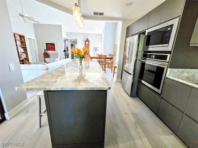 kitchen with ceiling fan, stainless steel appliances, decorative light fixtures, a breakfast bar, and light wood-type flooring