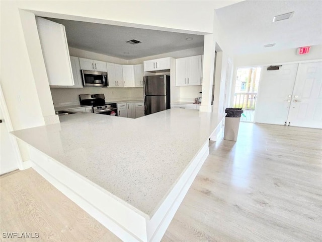 kitchen with white cabinets, light hardwood / wood-style floors, kitchen peninsula, and appliances with stainless steel finishes