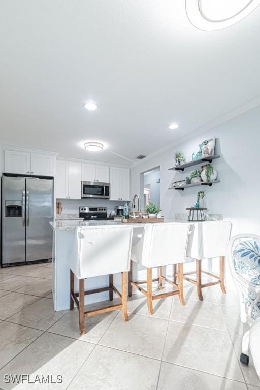 kitchen with white cabinetry, stainless steel appliances, crown molding, a breakfast bar area, and light tile patterned flooring