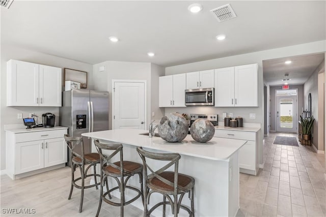 kitchen with light countertops, appliances with stainless steel finishes, a center island with sink, and white cabinetry