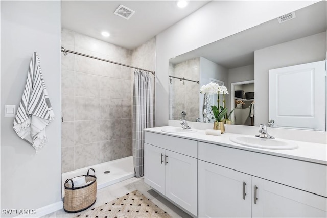 full bath with double vanity, visible vents, a sink, and tiled shower