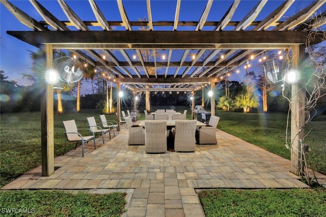 patio at night featuring a pergola and a lawn