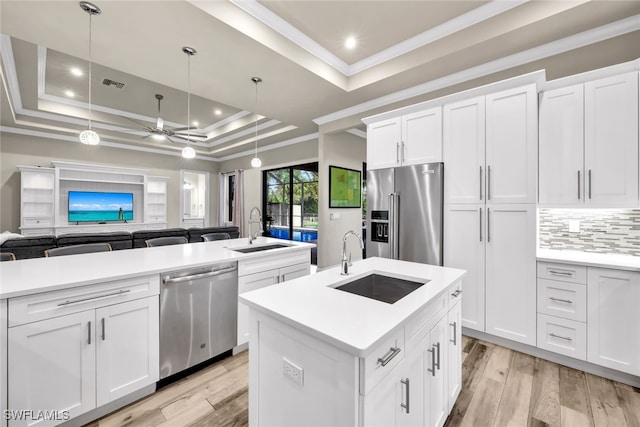 kitchen with stainless steel appliances, a raised ceiling, sink, decorative light fixtures, and an island with sink