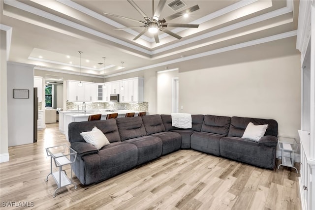 living room featuring ceiling fan, a raised ceiling, light wood-type flooring, and ornamental molding