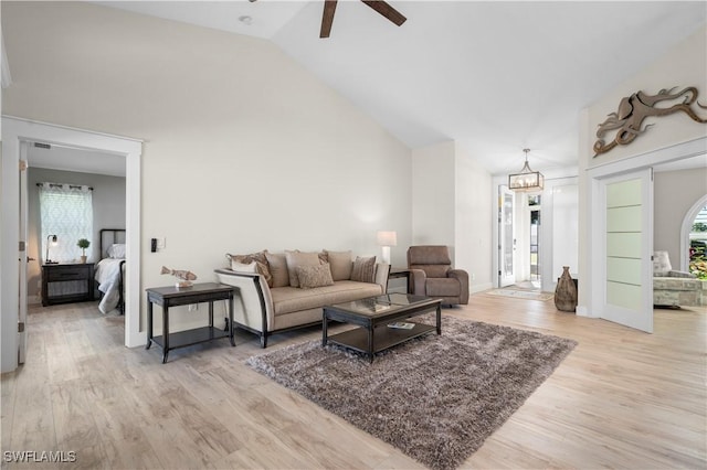 living room featuring ceiling fan with notable chandelier, light wood-type flooring, high vaulted ceiling, and plenty of natural light