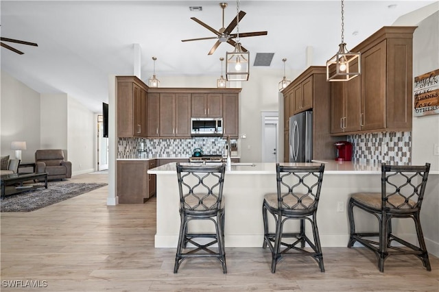 kitchen featuring backsplash, hanging light fixtures, a breakfast bar area, and appliances with stainless steel finishes