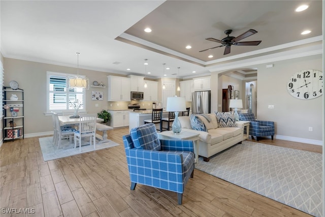 living room featuring light hardwood / wood-style floors, ceiling fan, ornamental molding, and a tray ceiling