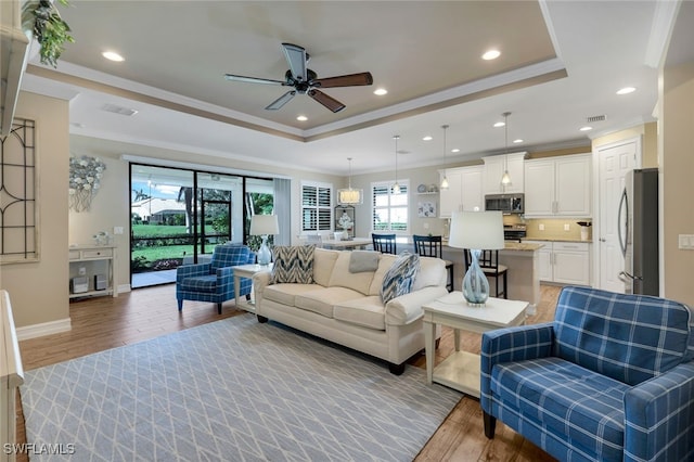 living room with light wood-type flooring, a tray ceiling, ceiling fan, and ornamental molding