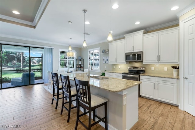 kitchen featuring a kitchen island with sink, sink, appliances with stainless steel finishes, decorative light fixtures, and white cabinetry