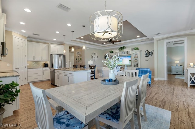 dining room with a chandelier, a tray ceiling, crown molding, and light hardwood / wood-style floors