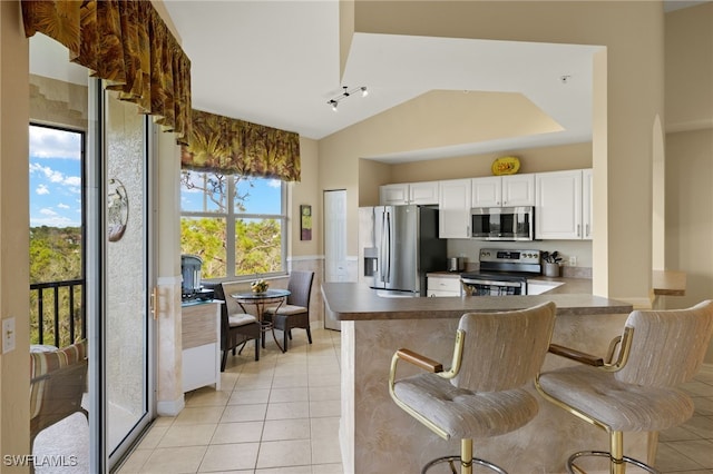 kitchen featuring a breakfast bar, kitchen peninsula, white cabinetry, stainless steel appliances, and light tile patterned floors