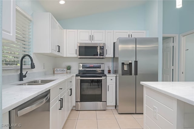 kitchen with appliances with stainless steel finishes, vaulted ceiling, sink, light tile patterned floors, and white cabinetry