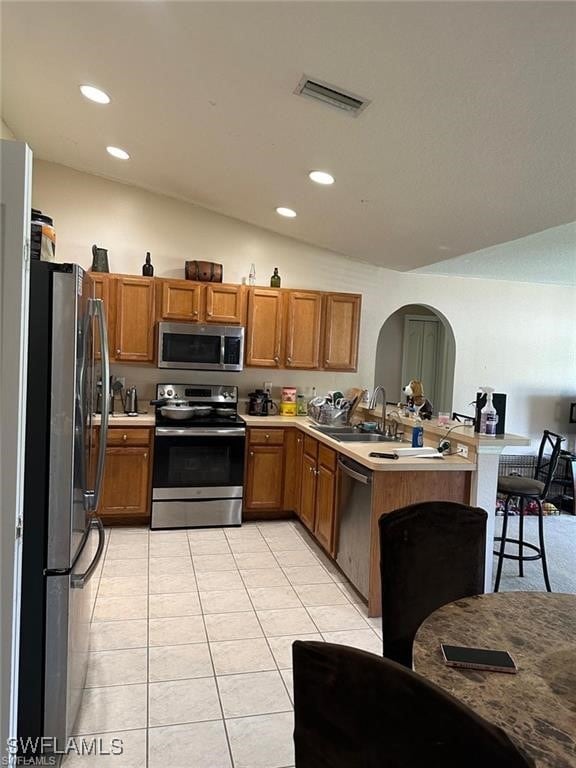 kitchen with kitchen peninsula, stainless steel appliances, sink, light tile patterned floors, and lofted ceiling