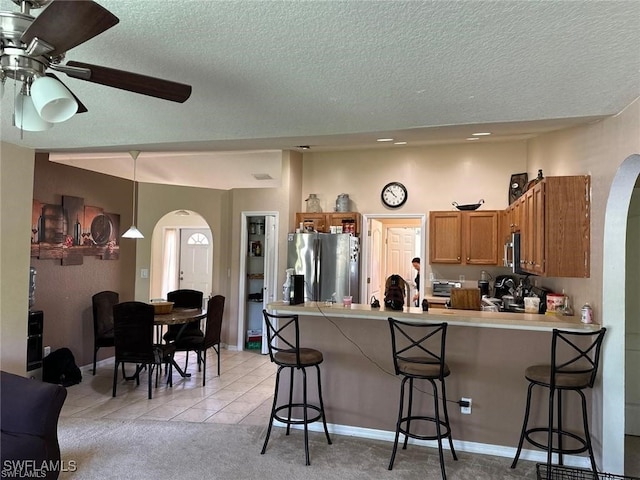 kitchen with ceiling fan, kitchen peninsula, a breakfast bar area, light tile patterned flooring, and appliances with stainless steel finishes