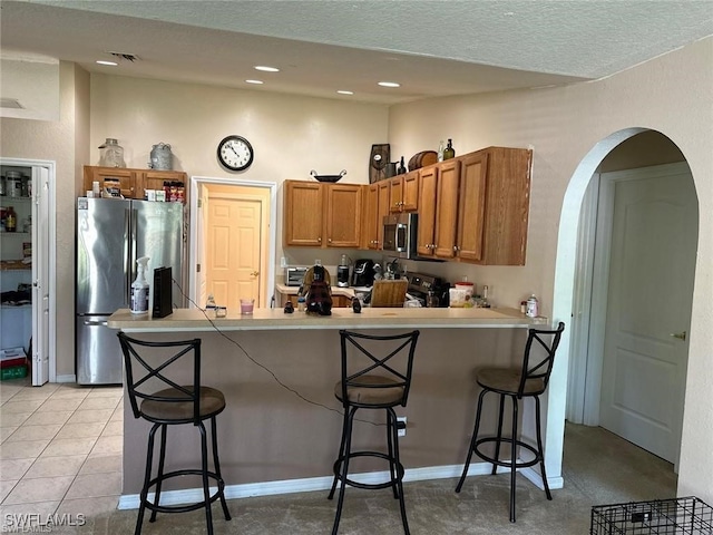 kitchen featuring stainless steel appliances, a kitchen breakfast bar, kitchen peninsula, a textured ceiling, and light tile patterned flooring