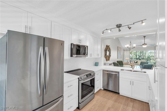 kitchen with sink, vaulted ceiling, a textured ceiling, appliances with stainless steel finishes, and white cabinets