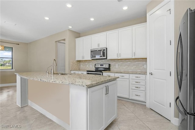 kitchen featuring stainless steel appliances, a sink, white cabinetry, decorative backsplash, and a center island with sink