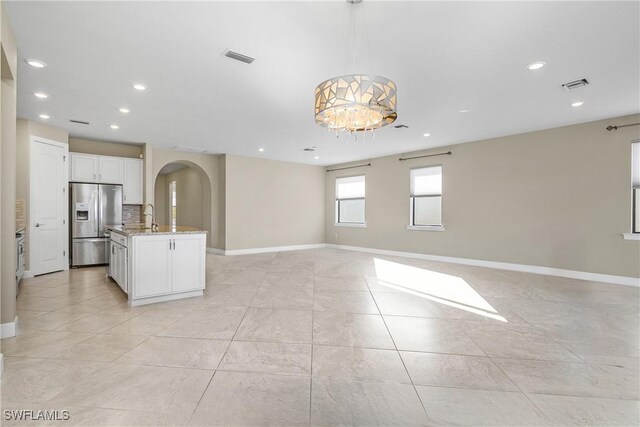 kitchen featuring white cabinetry, hanging light fixtures, stainless steel fridge with ice dispenser, a chandelier, and a center island with sink