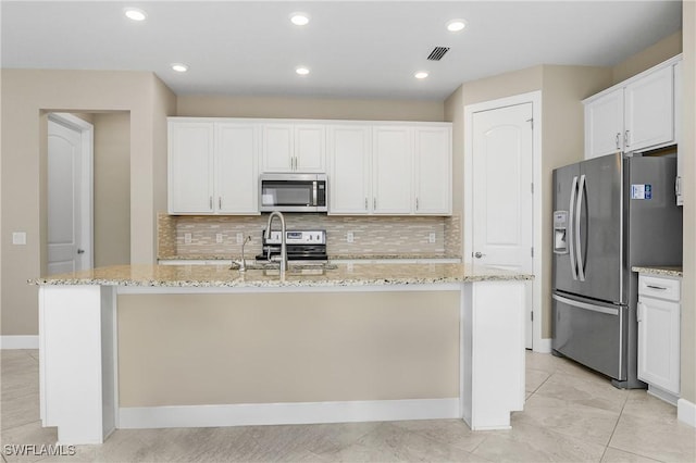 kitchen with an island with sink, light stone countertops, white cabinetry, and appliances with stainless steel finishes