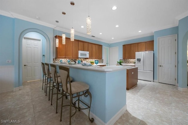 kitchen with crown molding, hanging light fixtures, a kitchen island, white appliances, and decorative backsplash