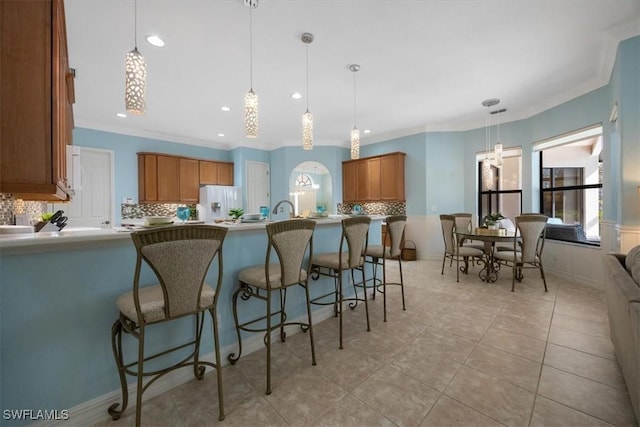 kitchen with decorative light fixtures, light tile patterned floors, tasteful backsplash, brown cabinetry, and a kitchen bar