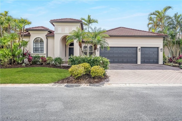 mediterranean / spanish-style house with decorative driveway, an attached garage, a tile roof, and stucco siding