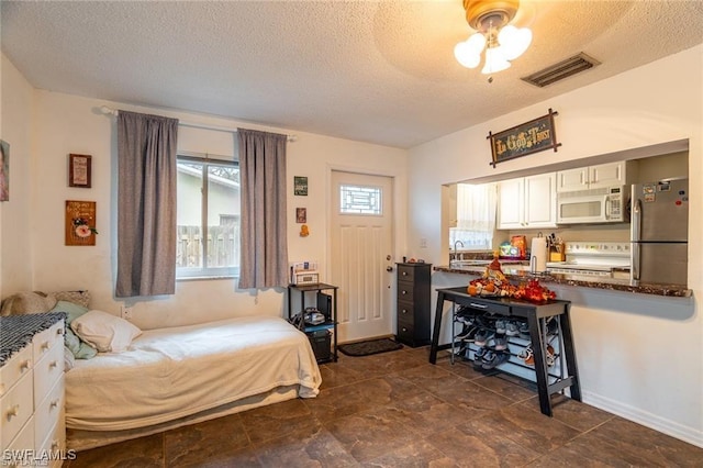 bedroom with stainless steel fridge, ceiling fan, multiple windows, and a textured ceiling