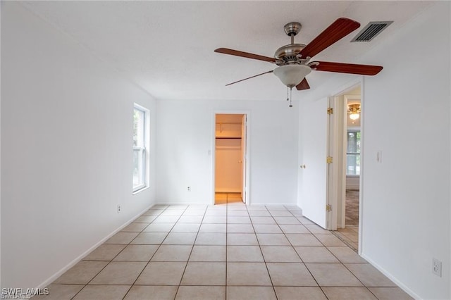 empty room with ceiling fan, light tile patterned floors, and a wealth of natural light