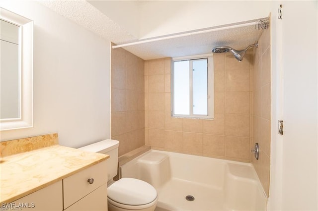 bathroom with vanity, toilet, tiled shower, and a textured ceiling