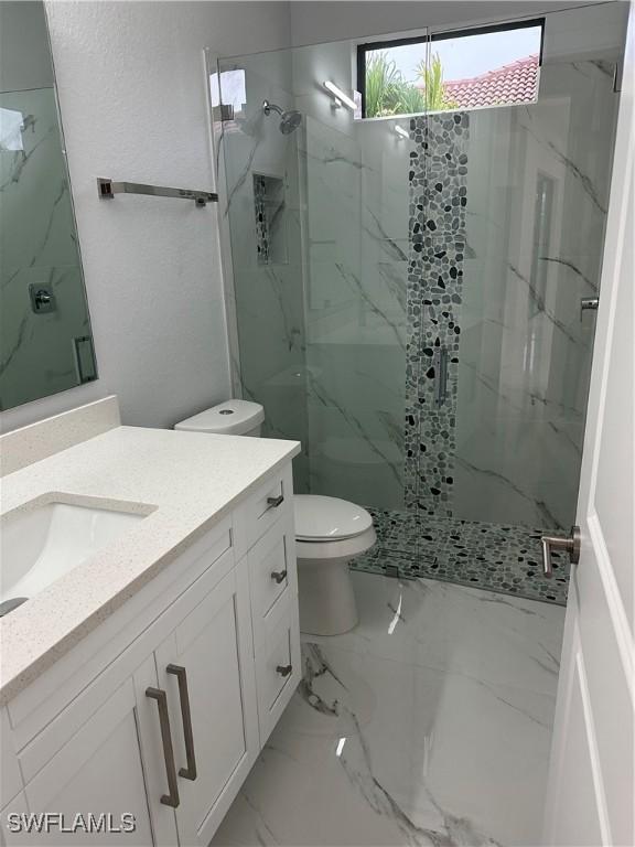 bathroom with tiled shower, vanity, and toilet