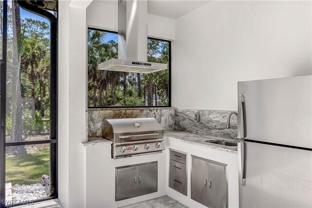 interior space with sink, stainless steel fridge, a wealth of natural light, light stone counters, and island exhaust hood