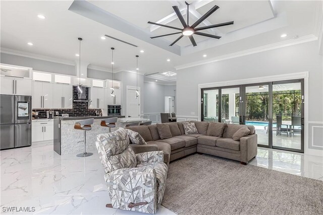 living room featuring a raised ceiling, ceiling fan, and ornamental molding