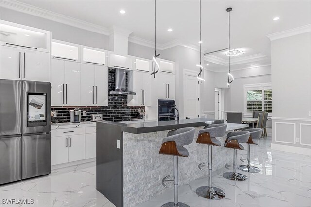 kitchen with white cabinetry, wall chimney range hood, stainless steel fridge, pendant lighting, and a center island with sink