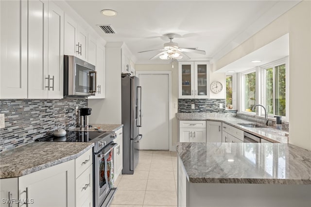 kitchen with kitchen peninsula, appliances with stainless steel finishes, sink, light tile patterned floors, and white cabinetry