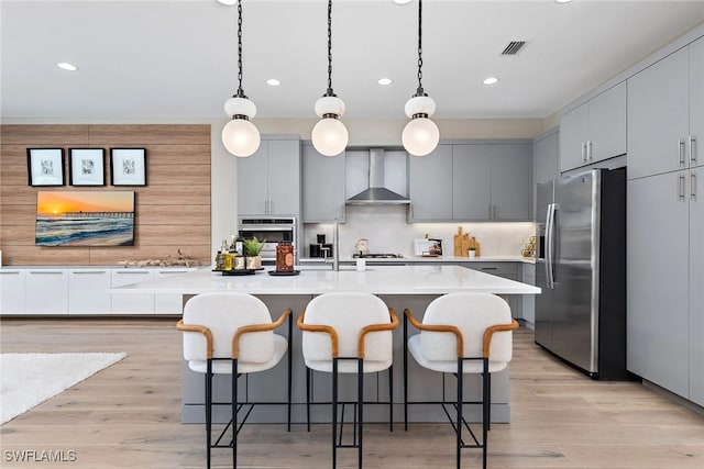 kitchen featuring stainless steel fridge with ice dispenser, gray cabinetry, wall chimney range hood, and an island with sink