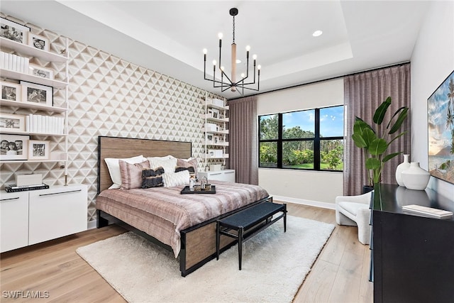 bedroom featuring a notable chandelier, a raised ceiling, and light wood-type flooring