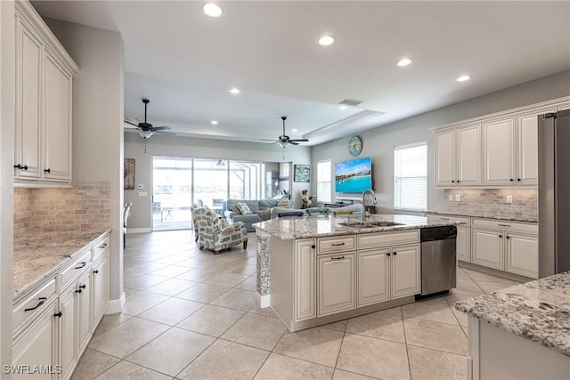 kitchen with dishwasher, sink, light stone countertops, an island with sink, and white cabinetry