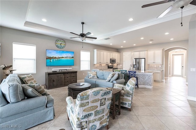 tiled living room with crown molding, sink, a tray ceiling, and ceiling fan