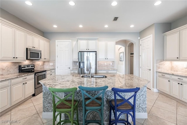 kitchen with light tile patterned flooring, a breakfast bar, an island with sink, light stone counters, and stainless steel appliances