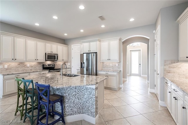 kitchen with stainless steel appliances, a kitchen island with sink, sink, and light stone countertops