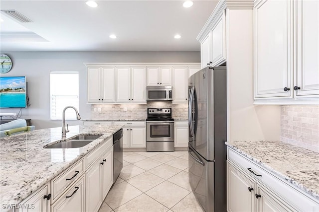 kitchen with appliances with stainless steel finishes, light stone counters, sink, light tile patterned floors, and white cabinetry