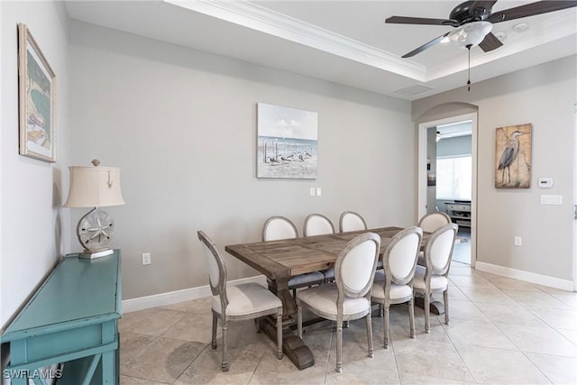 tiled dining space with ceiling fan, a raised ceiling, and crown molding