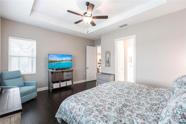 bedroom with ceiling fan, dark hardwood / wood-style floors, a raised ceiling, and ensuite bath