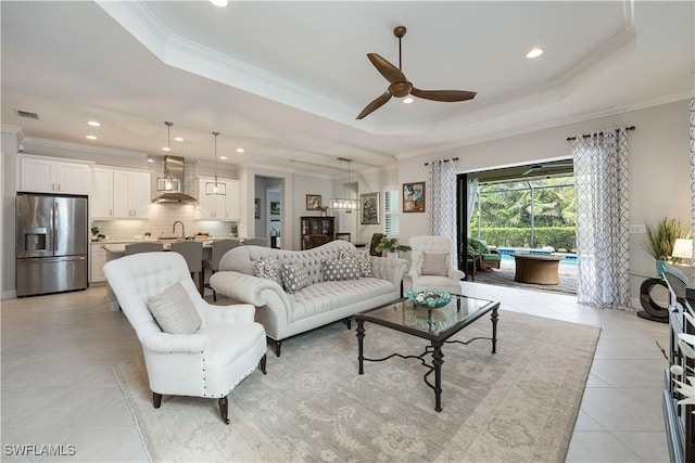 living room with ceiling fan, light tile patterned floors, ornamental molding, and a tray ceiling