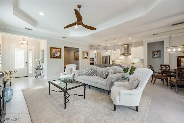 living room featuring ceiling fan, light tile patterned flooring, crown molding, and a raised ceiling