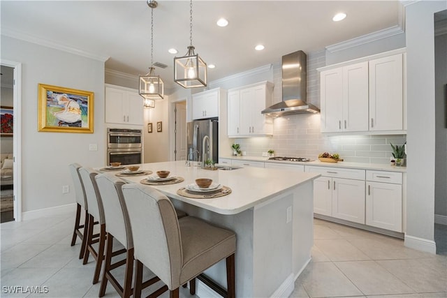 kitchen featuring pendant lighting, white cabinetry, wall chimney range hood, stainless steel appliances, and an island with sink