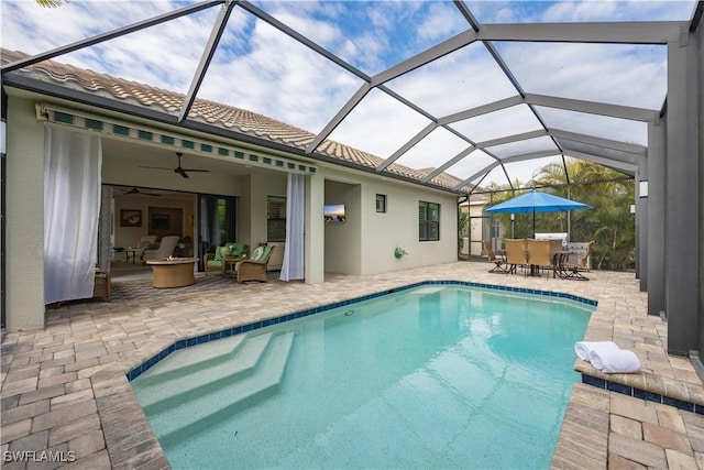 view of swimming pool featuring ceiling fan, glass enclosure, an outdoor living space with a fire pit, and a patio