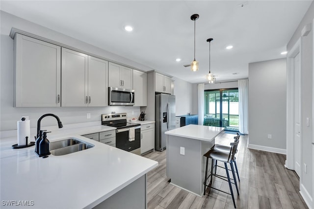 kitchen with appliances with stainless steel finishes, a kitchen island, light wood-style floors, and a sink