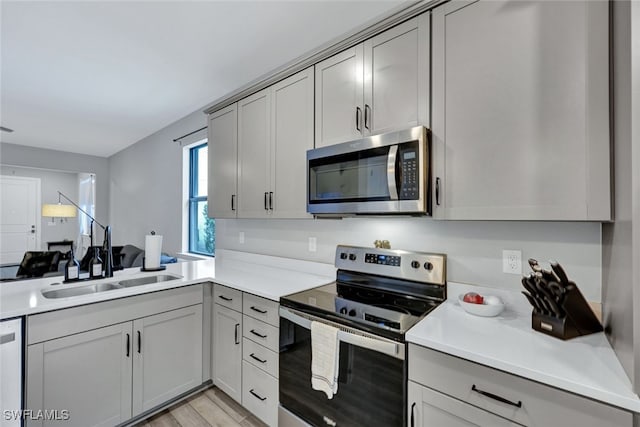 kitchen featuring gray cabinetry, light countertops, light wood-style flooring, appliances with stainless steel finishes, and a sink