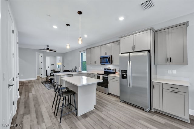 kitchen with a peninsula, gray cabinets, a sink, stainless steel appliances, and light countertops